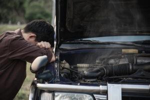 A stressed and sad man next to a broken car. Read this article to find out signs your car is a lemon. Never skip a pre-purchase car inspection in Melbourne. Call German Precision today!